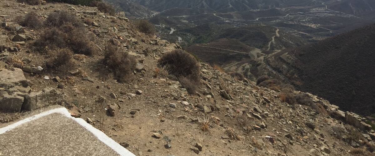 A mountainous landscape with a winding road, rocky terrain, and a distant view of a valley and a body of water.