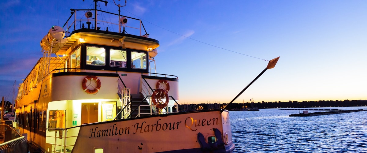 Un bateau nommé « Hamilton Harbour Queen » était amarré à un quai, sous un ciel dégagé et sur une eau calme.