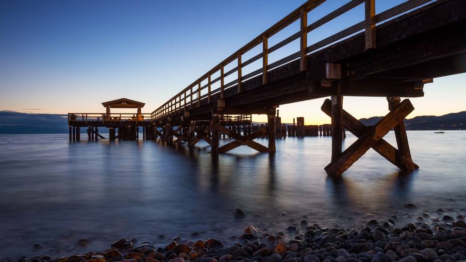 A wooden pier extending over calm water with a rocky shoreline.