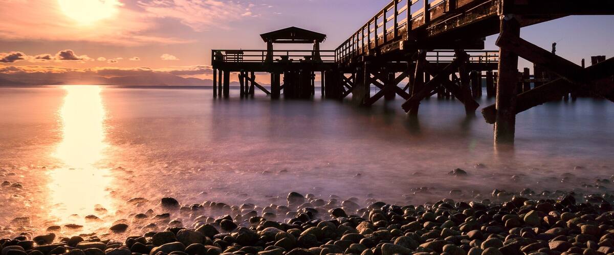 A wooden pier extending into calm waters at sunset.