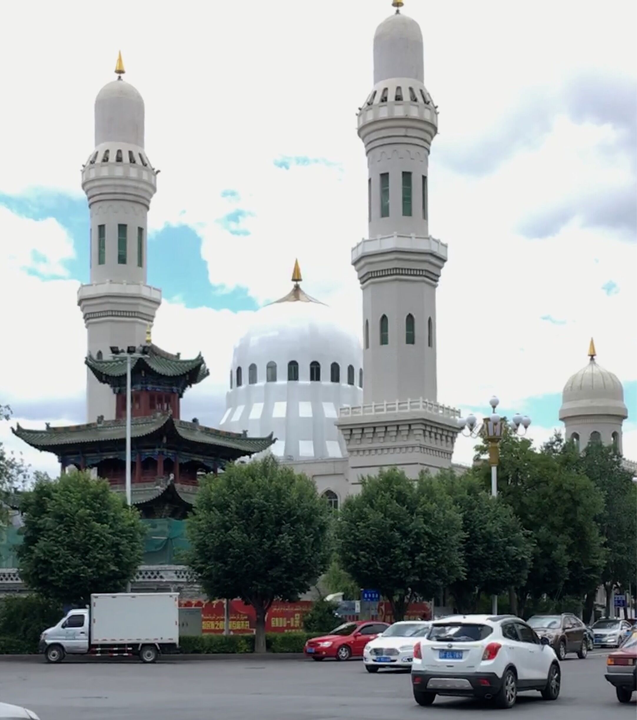 A mosque with two minarets and a large central dome, surrounded by trees and a busy street with cars.