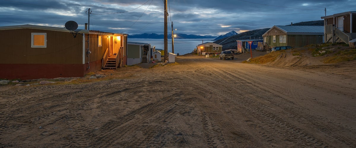 A dirt road in a remote area with small buildings and a mountain in the background.