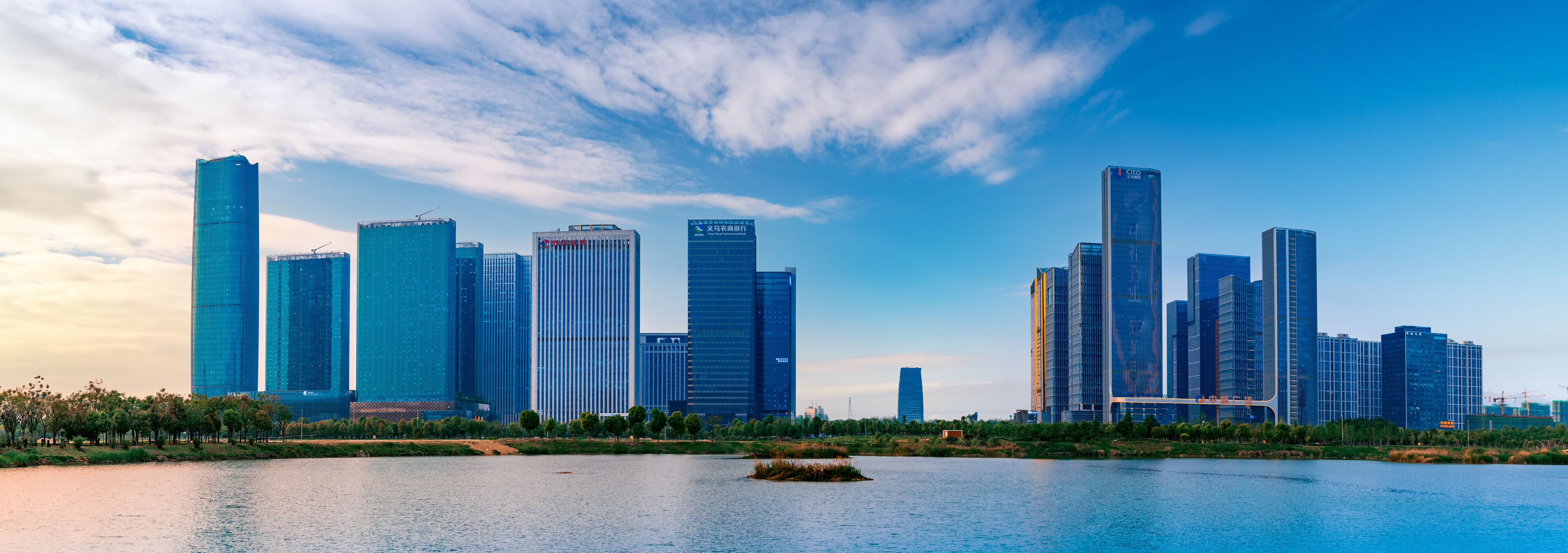 A city skyline with modern skyscrapers and a calm river in the foreground.