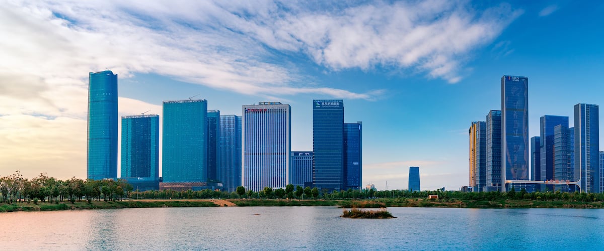 A city skyline with modern skyscrapers and a calm river in the foreground.