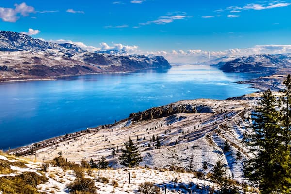 A snow-covered mountainous landscape with a large lake and clear blue sky.