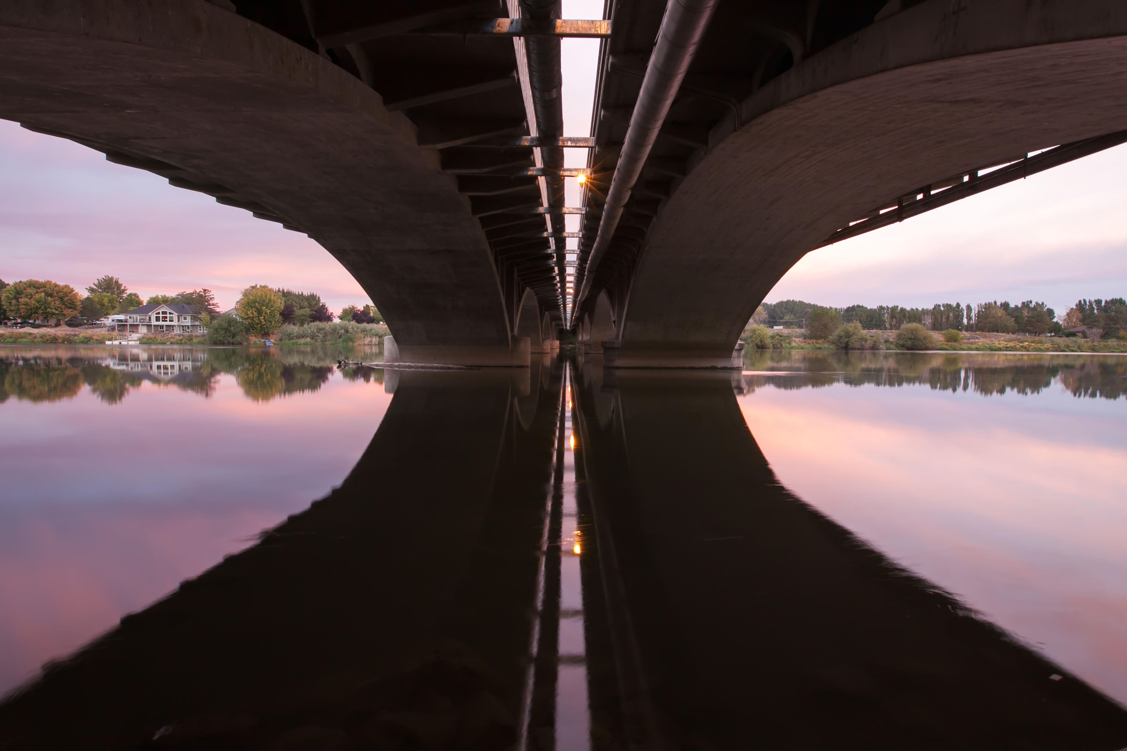 The underside of a bridge spanning the Yakima River, and the far shoreline and landscape at sunrise.; Yakima River, Prosser, Washington