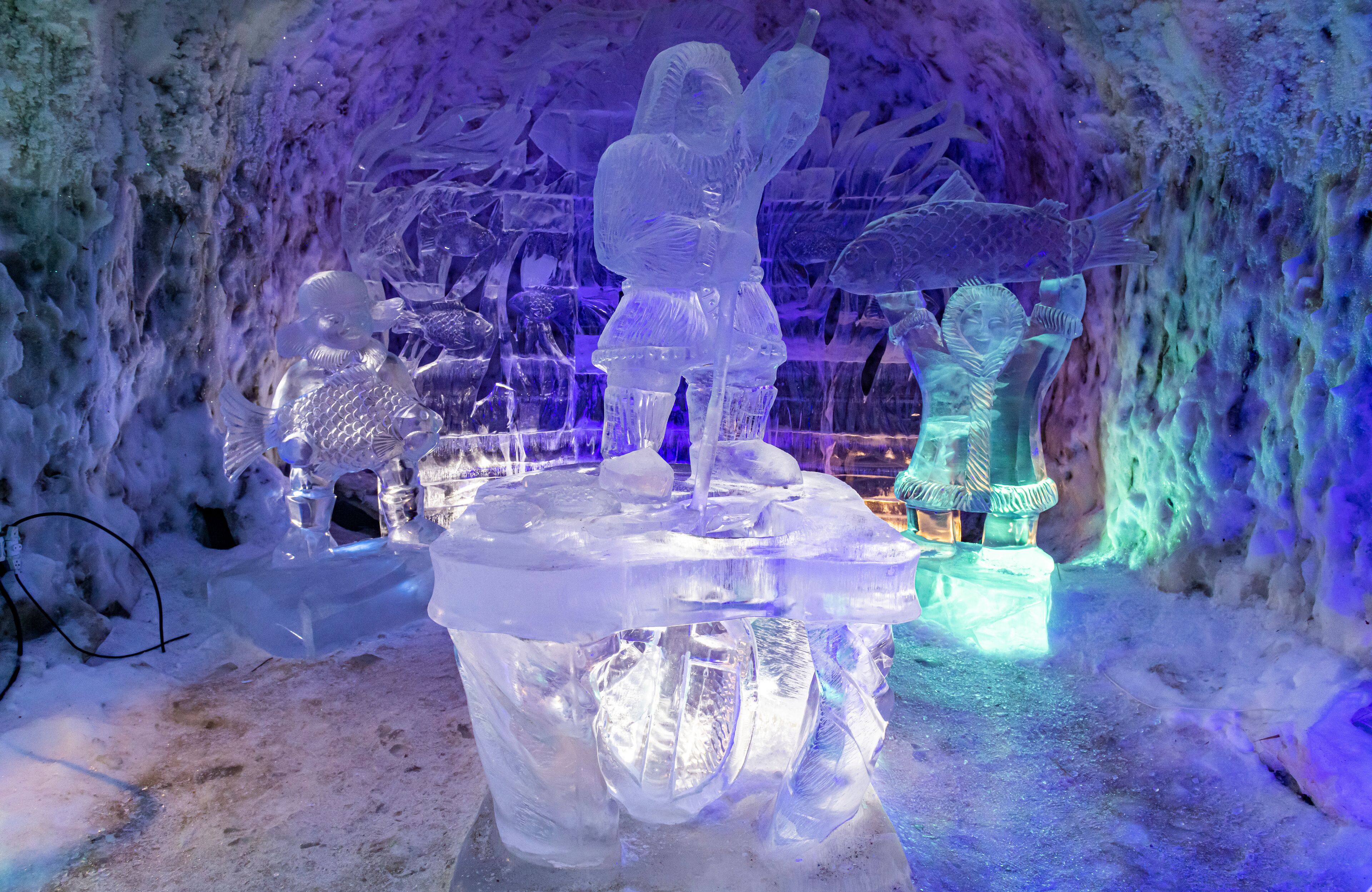 An ice sculpture display with figures and fish, illuminated by blue and purple lights.