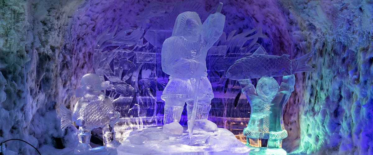 An ice sculpture display with figures and fish, illuminated by blue and purple lights.