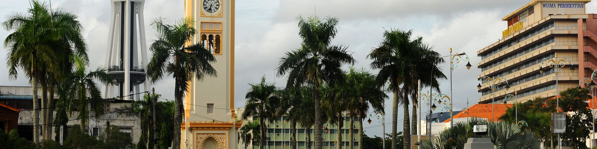 A tower with a clock, a modern tower, and palm trees.