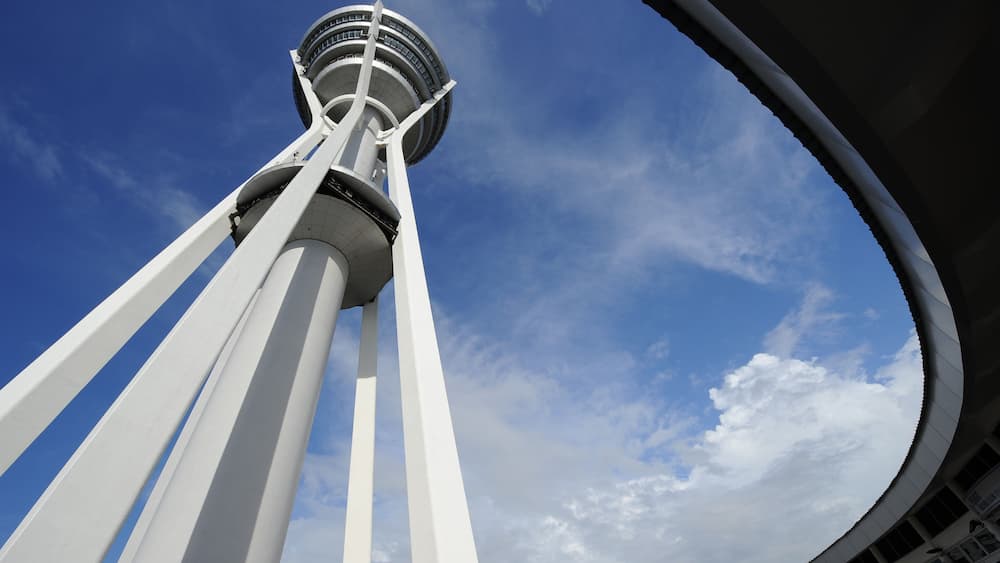 A tower with white structural elements and a circular observation deck against a blue sky with clouds.