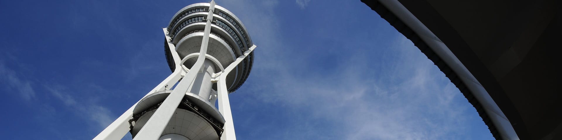 A tower with white structural elements and a circular observation deck against a blue sky with clouds.