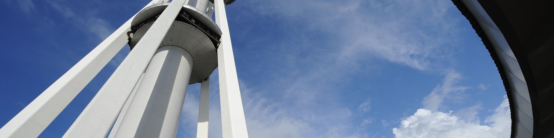Una torre con elementos estructurales blancos y una plataforma de observación circular contra un cielo azul con nubes.