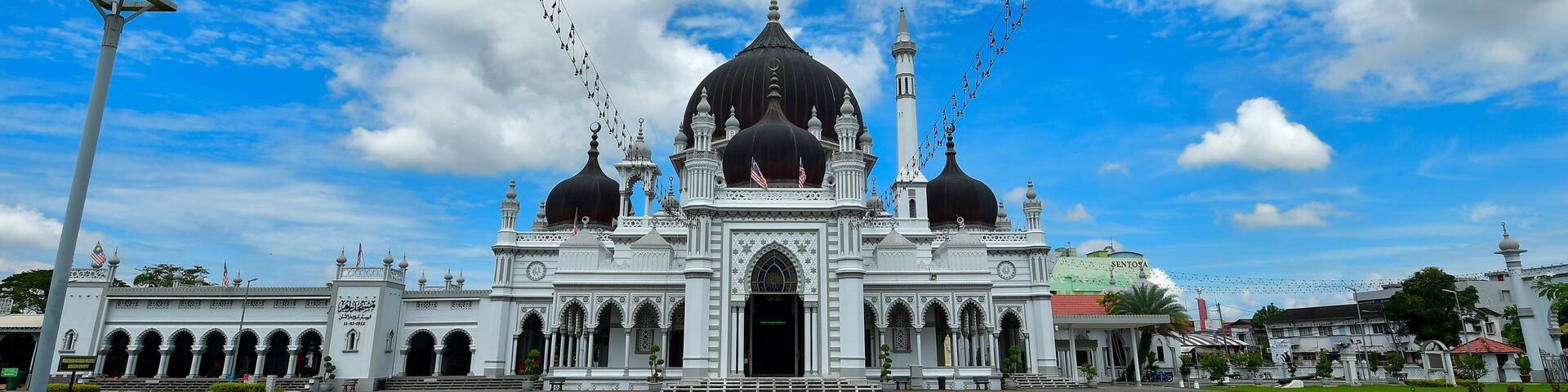 A large mosque with multiple domes and minarets, surrounded by a paved courtyard and greenery.