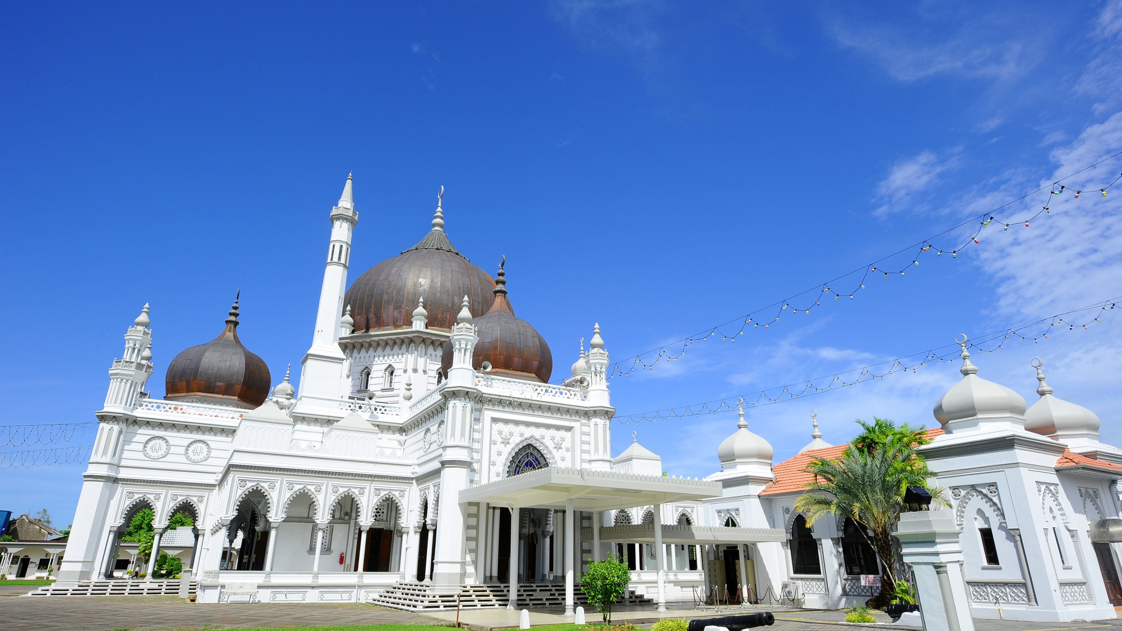 A white mosque with multiple domes and minarets under a clear blue sky.