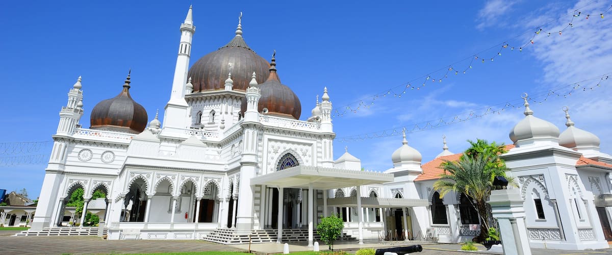 A white mosque with multiple domes and minarets under a clear blue sky.