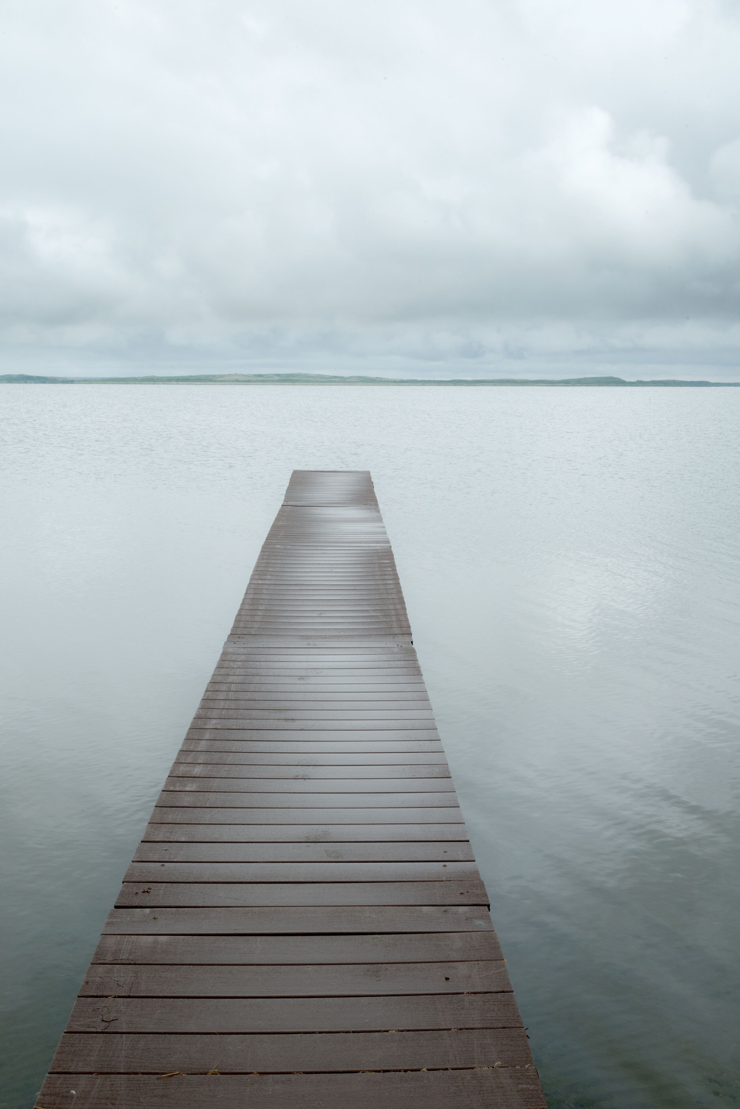 Canada, SK, Lloydminster, Manitou Lake.  Weathered wooden dock juts out into the still lake.