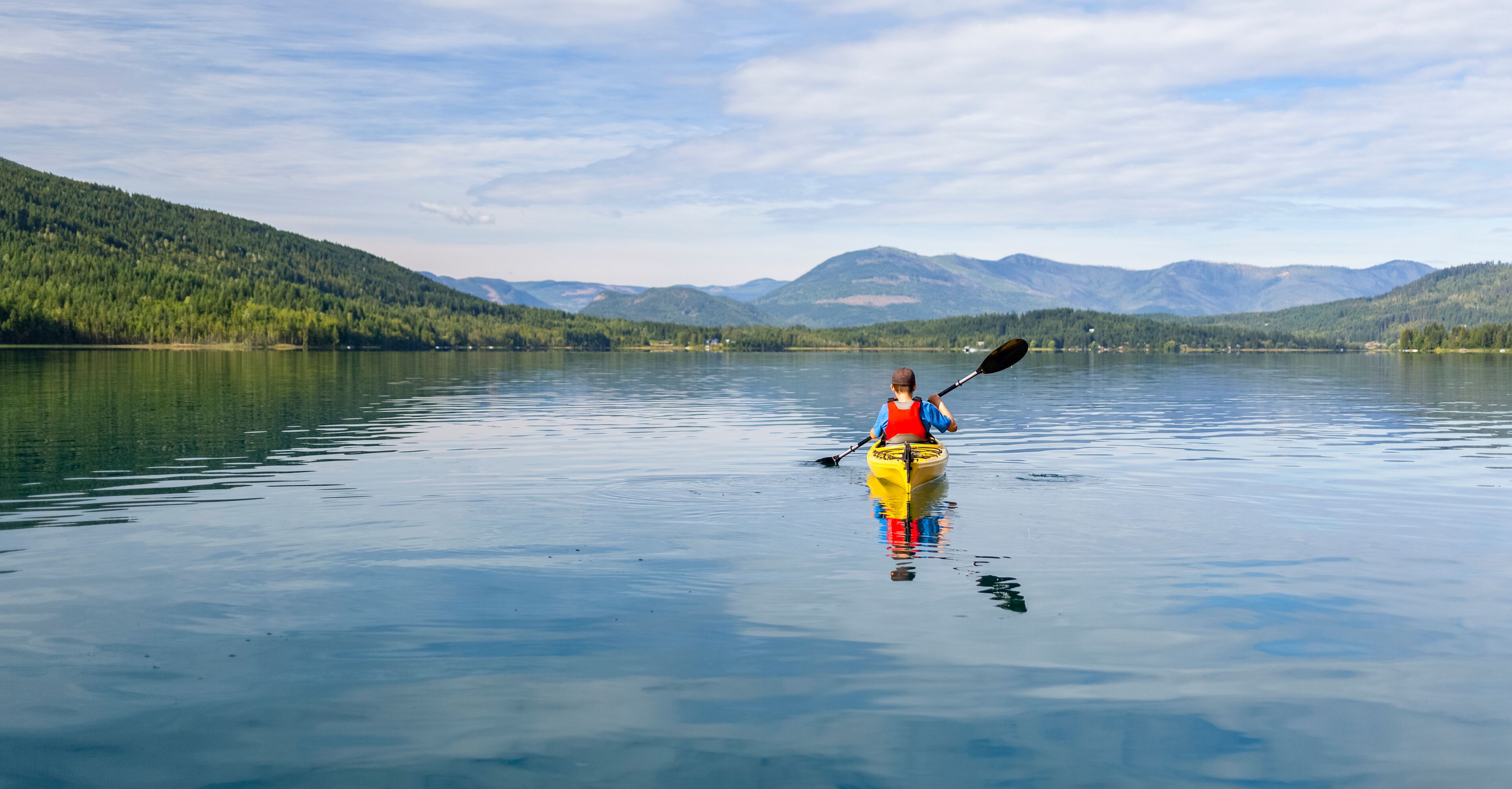 A kayaker in a yellow kayak on a calm lake with mountains in the background.