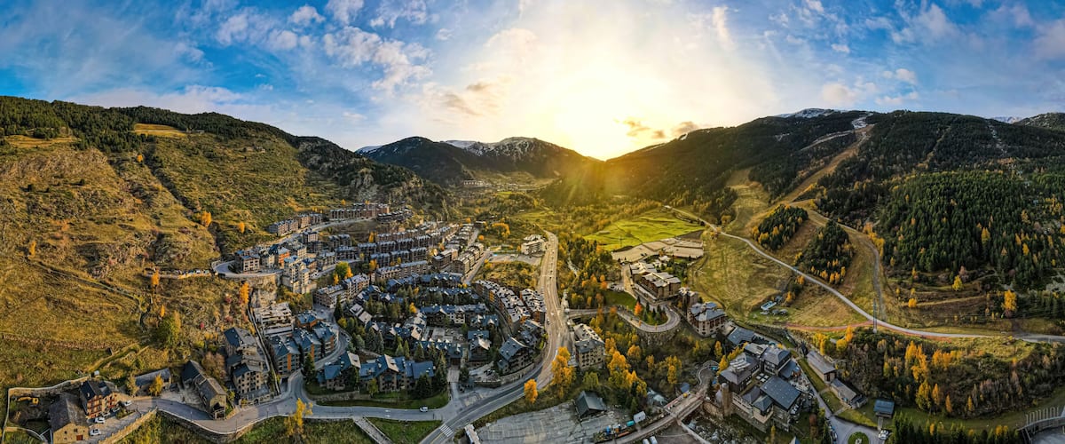 A panoramic view of a valley with a residential area, roads, and surrounding hills.