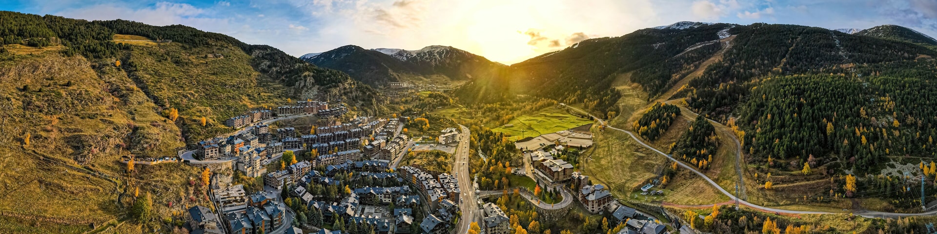 A panoramic view of a valley with a residential area, roads, and surrounding hills.