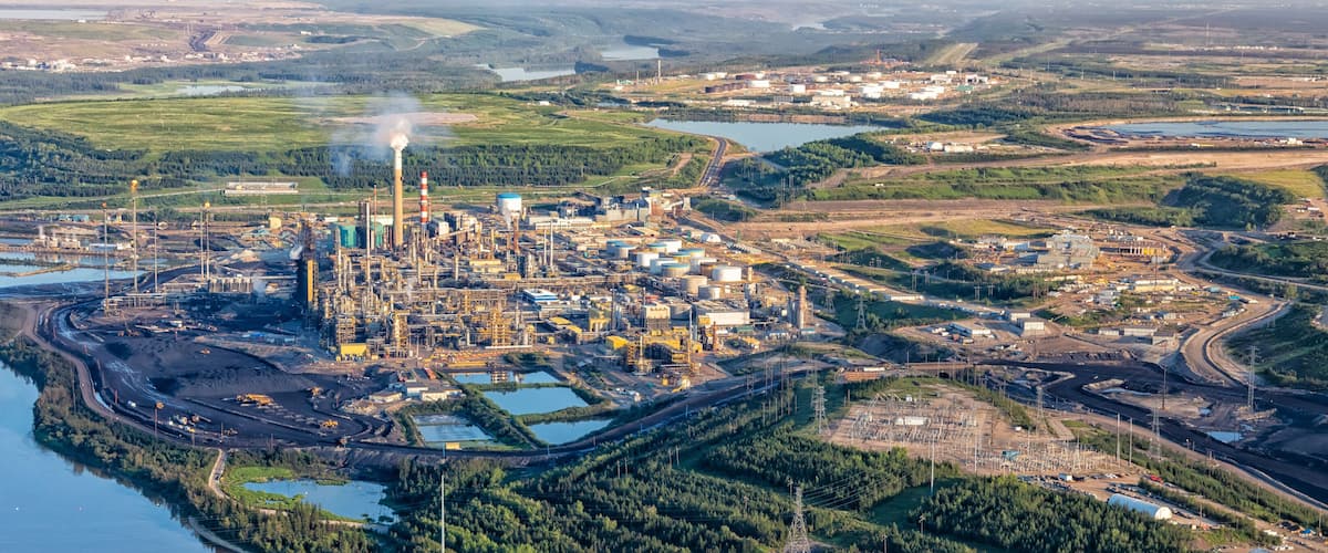 An industrial complex with multiple buildings, storage tanks, and a large body of water.