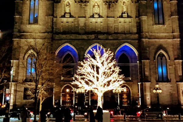 A historic church with illuminated windows and statues, surrounded by people and cars.