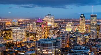 A cityscape at dusk with illuminated buildings and a bridge in the distance.
