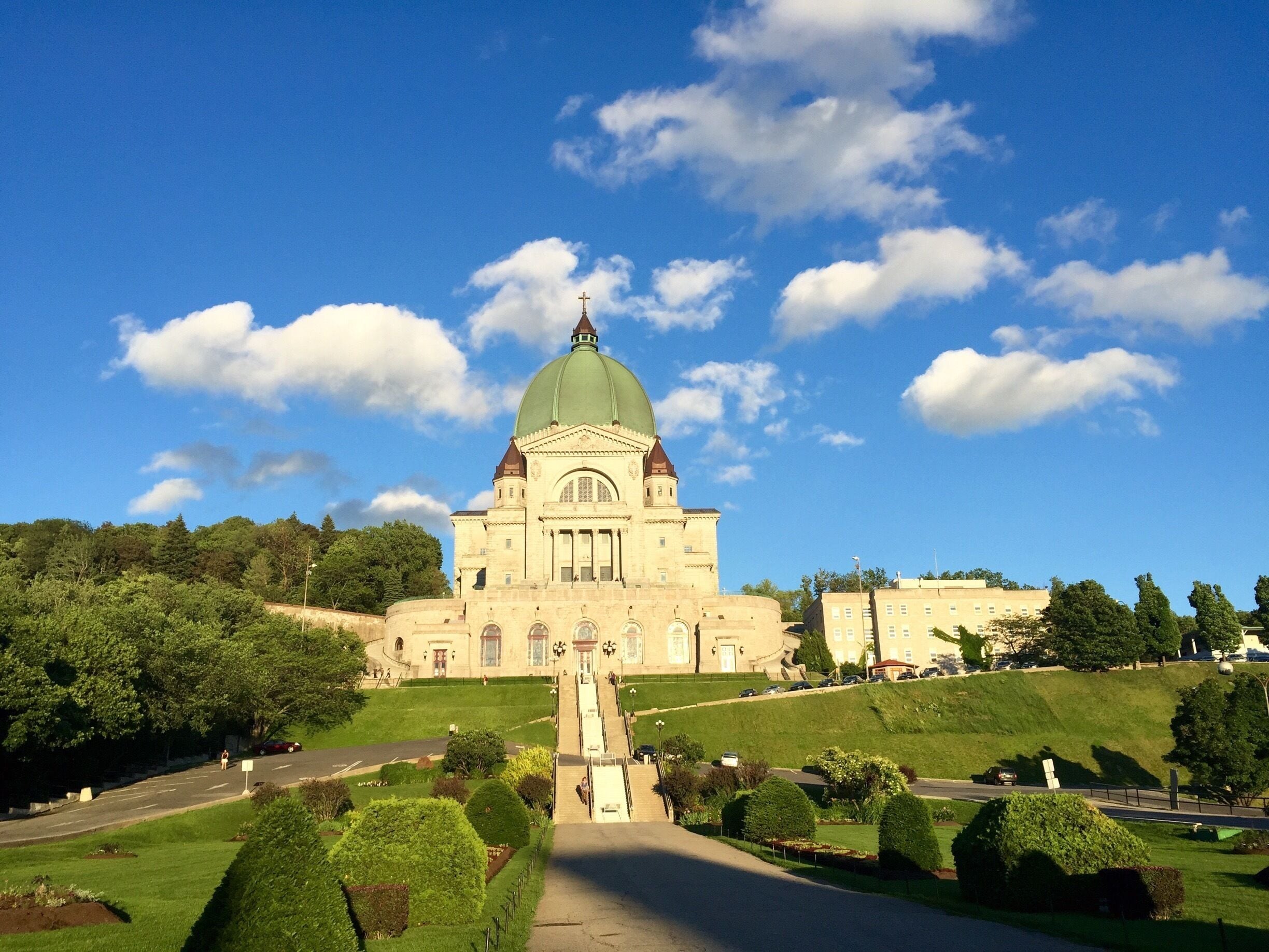 A large building with a green dome and a cross on top, surrounded by green lawns and trees.