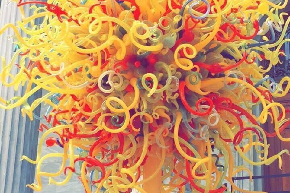 Een kleurrijke glazen sculptuur voor een klassiek gebouw met kolommen.