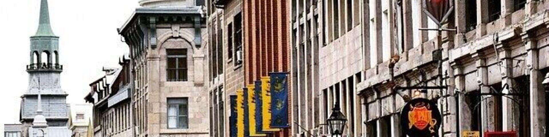 Uma rua de paralelepípedos flanqueada por edifícios históricos, um campanário de igreja e uma bandeira.