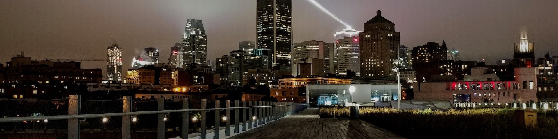 Une vue nocturne sur les gratte-ciel d’une ville, avec des bâtiments illuminés et une promenade en bois.