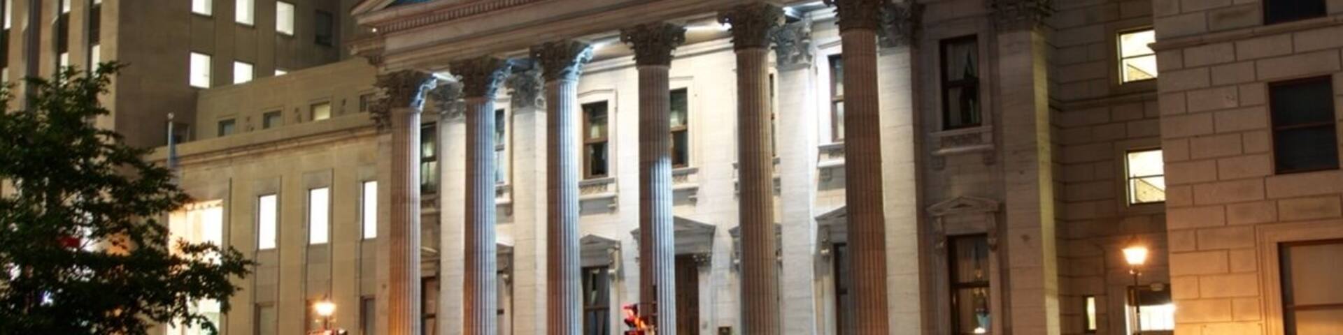 A classical building with columns and a blue-lit dome at dusk.