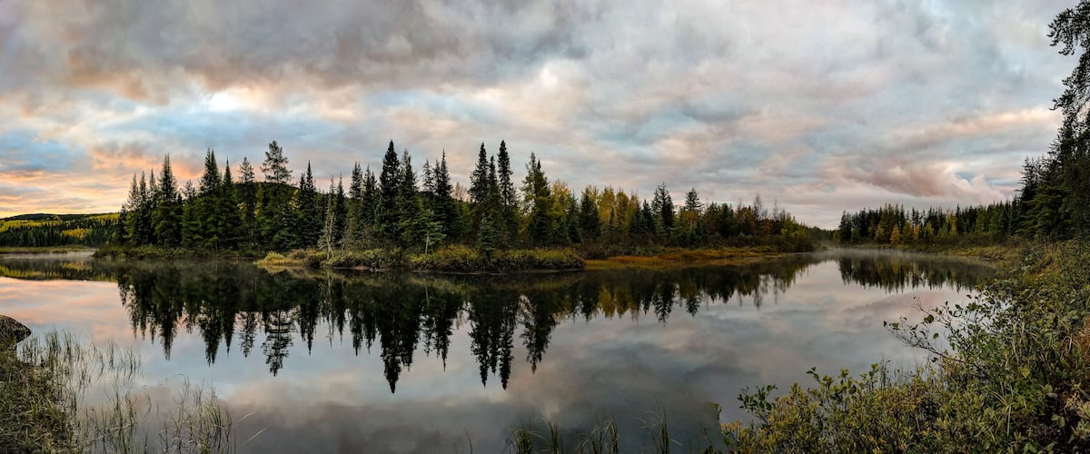 A calm lake surrounded by dense forest and a cloudy sky.