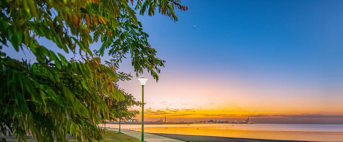 A sunset over a beach with a sidewalk and street lamps.