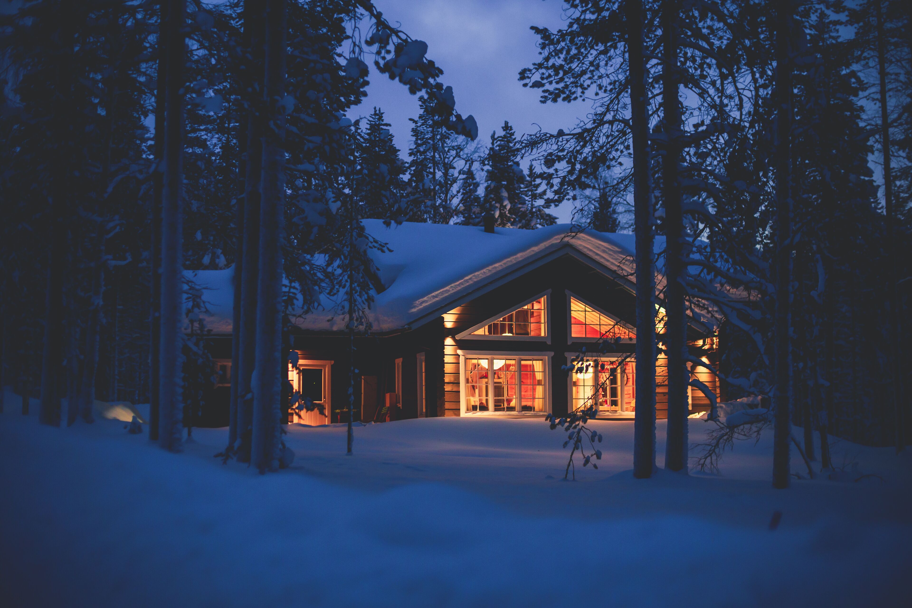 A cozy wooden cabin cottage chalet house covered in snow near ski resort in winter with the lights turn on