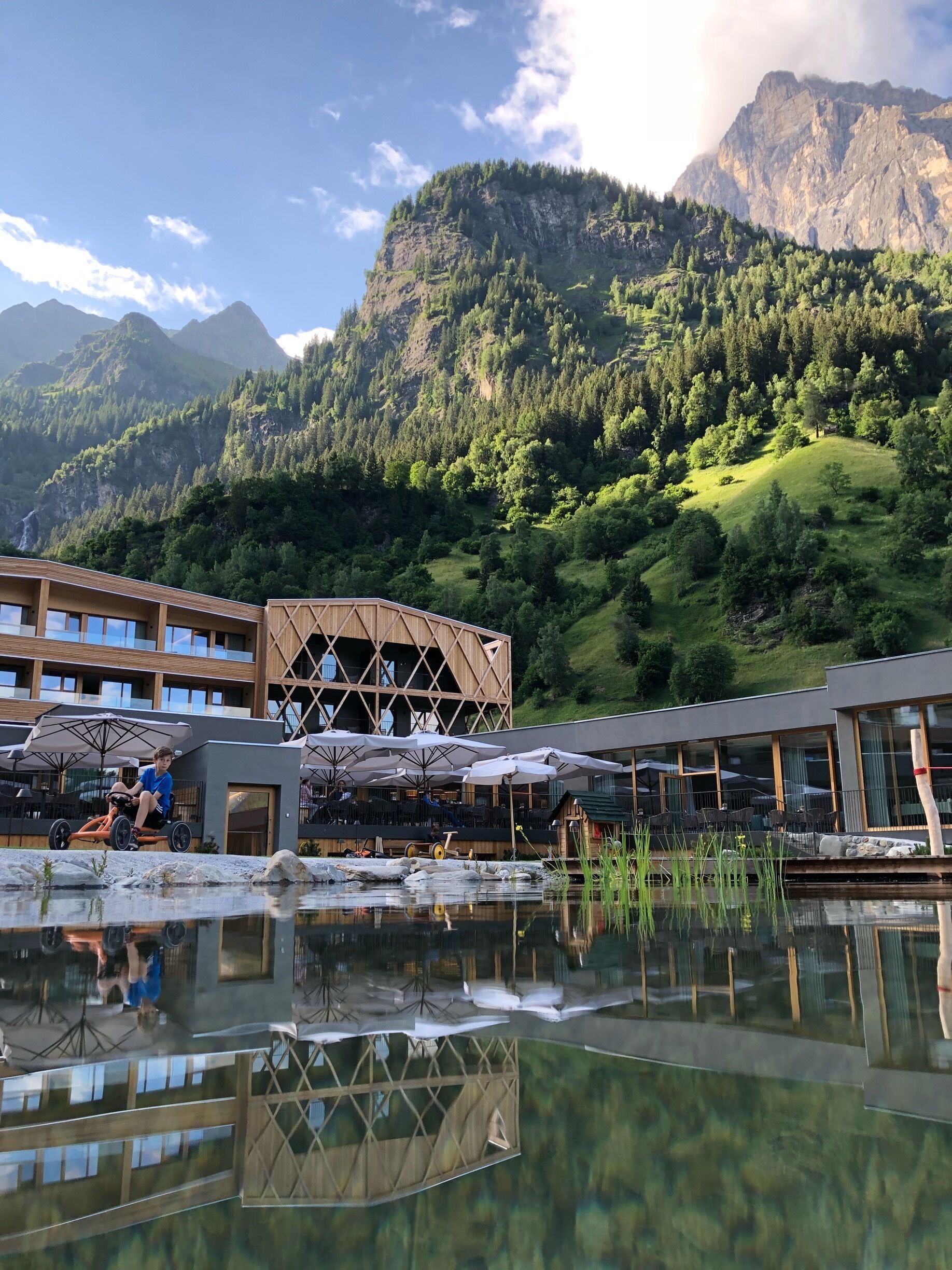 A lakeside resort with a wooden building, outdoor seating, and a mountain backdrop.