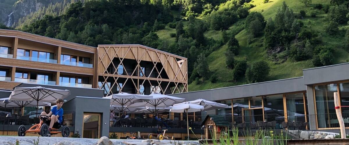 A lakeside resort with a wooden building, outdoor seating, and a mountain backdrop.