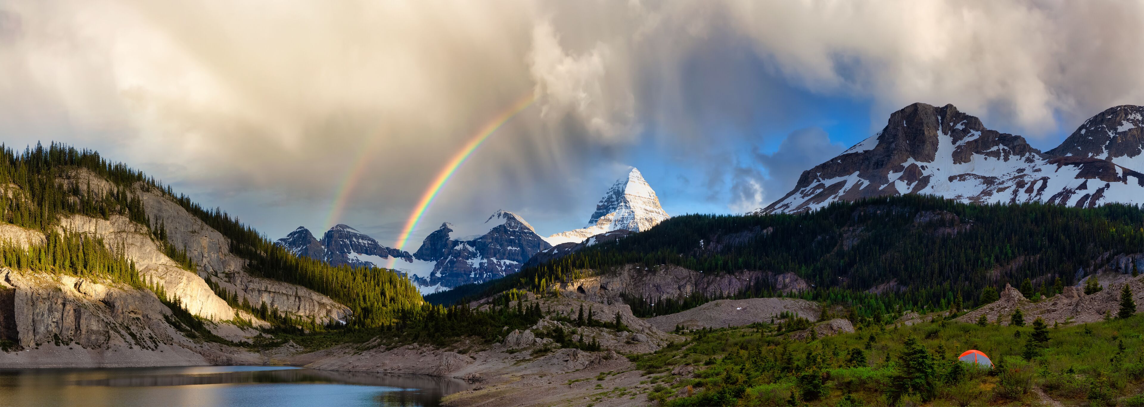 A mountain landscape with a rainbow, a lake, and a tent.