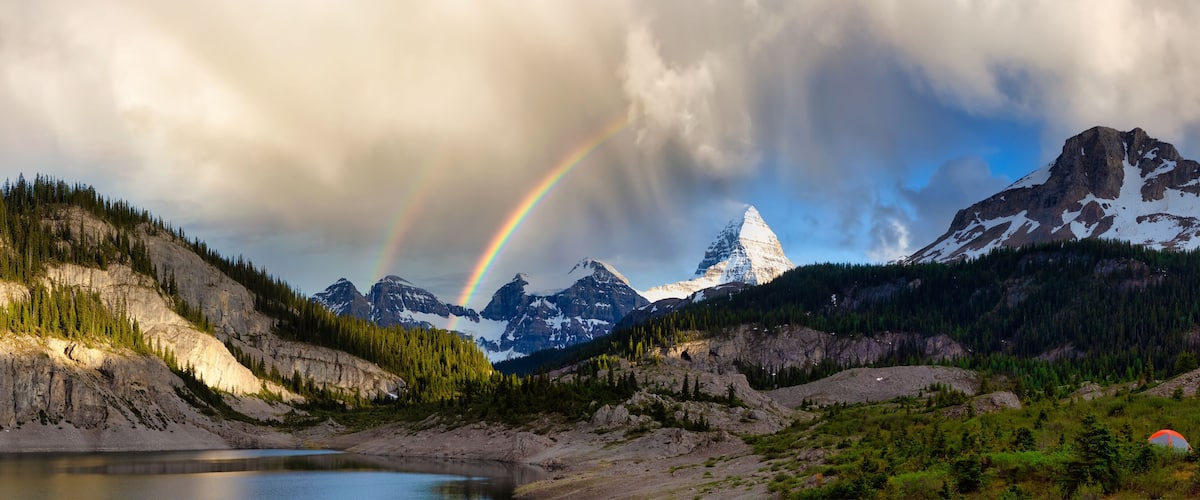 A mountain landscape with a rainbow, a lake, and a tent.