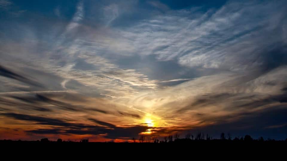 A sunset with clouds over a silhouette of trees.