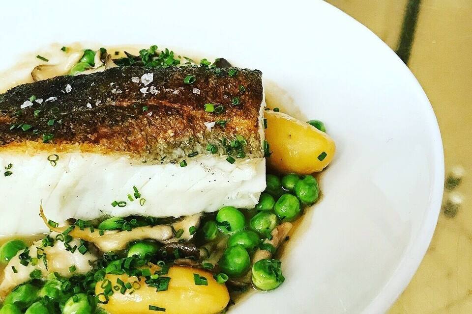 Un plato blanco con un trozo de pescado, guisantes verdes y patatas amarillas.