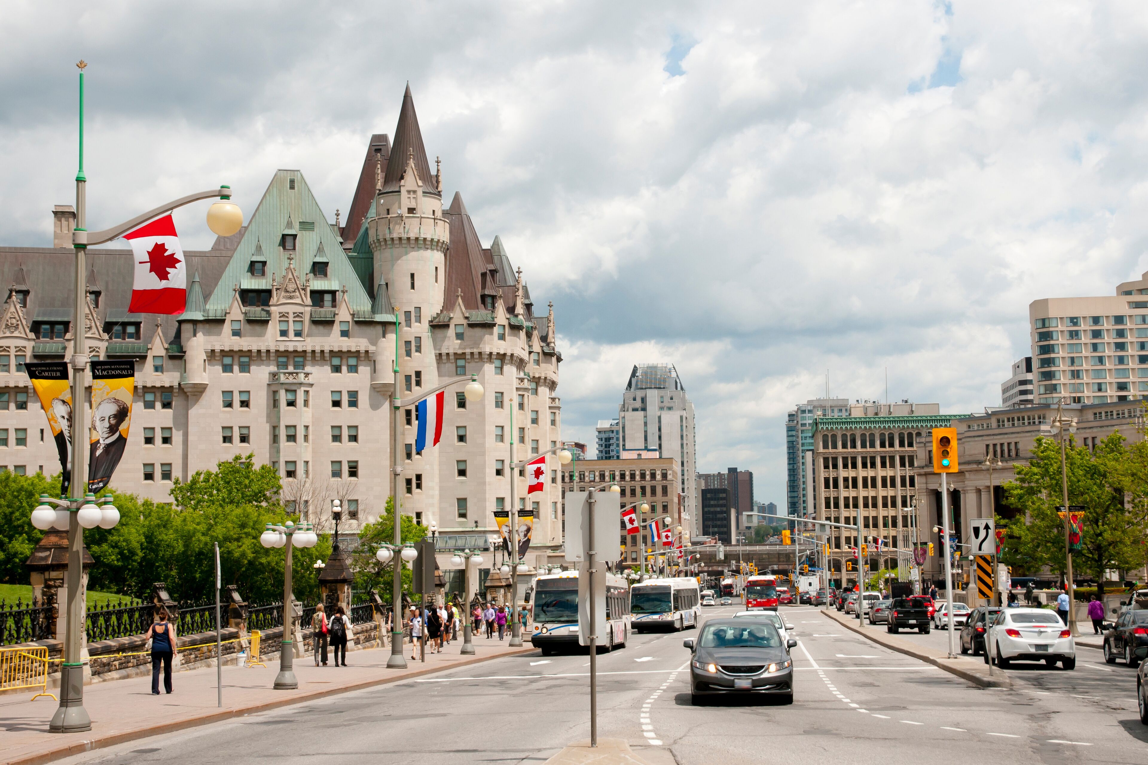 Una calle urbana con un edificio histórico que presenta una torre y varias banderas, incluida la bandera canadiense.
