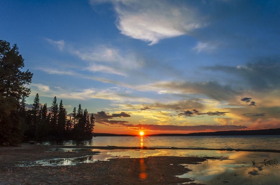 lake and red sunset glow, sun rays, black silhouettes of trees and reflection