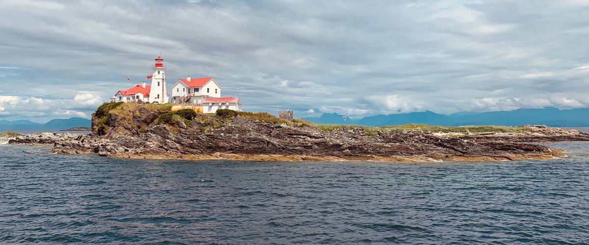 A lighthouse on a rocky island with red roofs, surrounded by calm waters and a cloudy sky.
