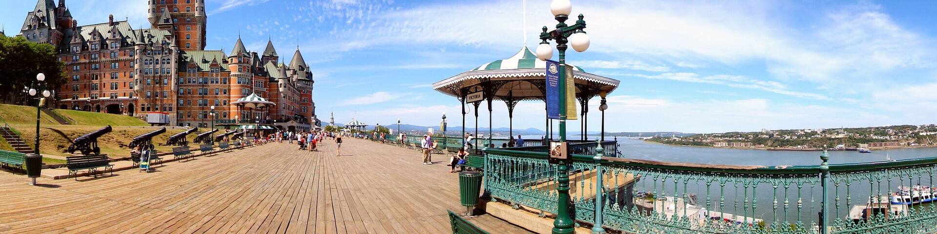 A historic building with a tower, a waterfront promenade, and a gazebo with a Canadian flag.