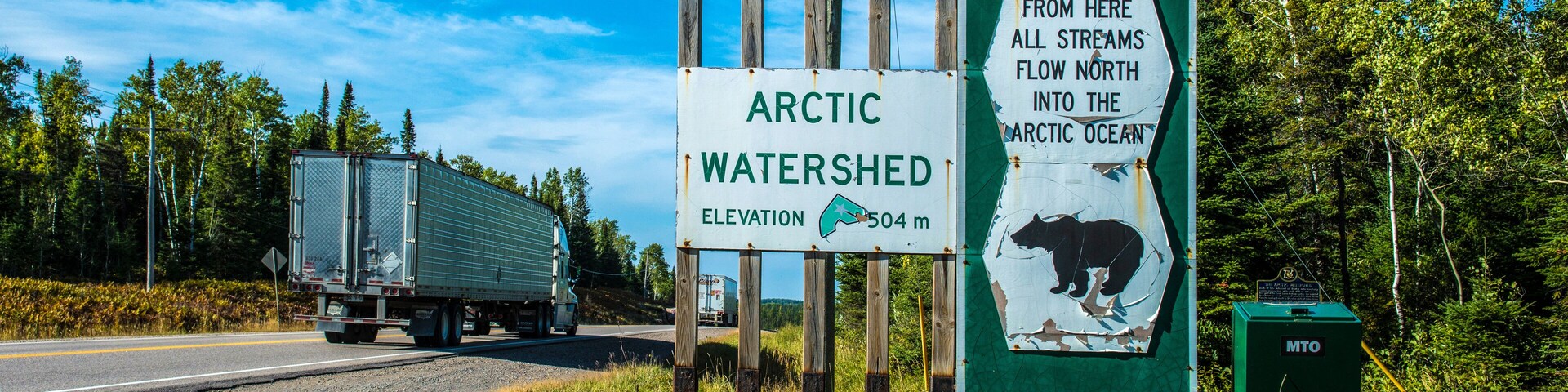 A road sign indicating the Arctic Watershed Elevation at 504 meters, with moose and bear illustrations.
