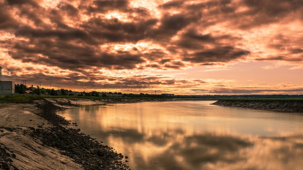 Petitcodiac River with dramatic sunrise cloudscape at Bore Park or Parc Bore Riverfront Walk, a popular place to watch the tidal bore in Moncton, New Brunswick, Canada