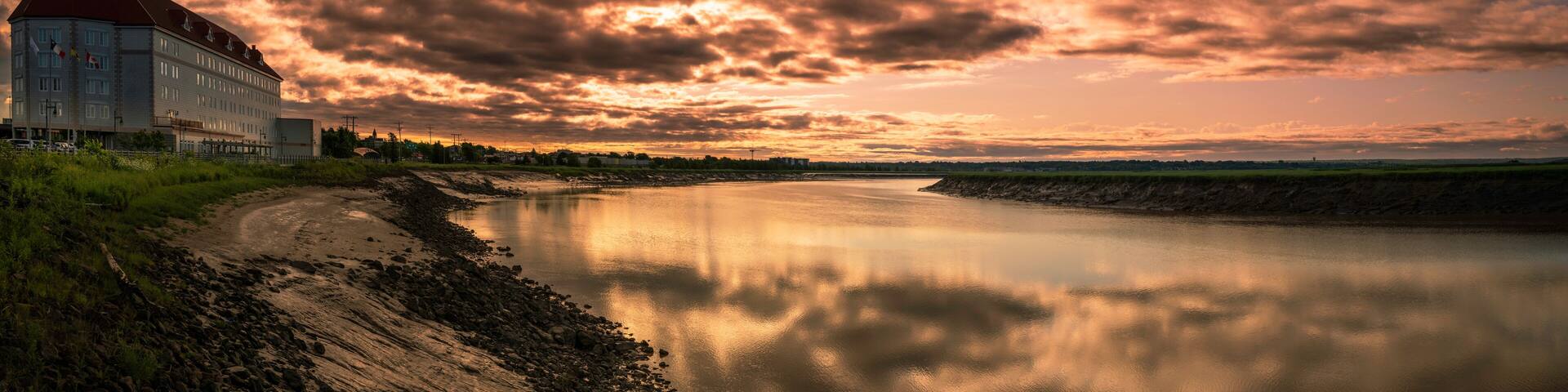 Petitcodiac River with dramatic sunrise cloudscape at Bore Park or Parc Bore Riverfront Walk, a popular place to watch the tidal bore in Moncton, New Brunswick, Canada