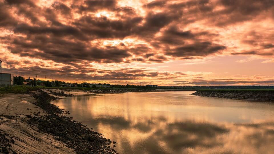 A riverside view with a large building and a dramatic sunset sky.