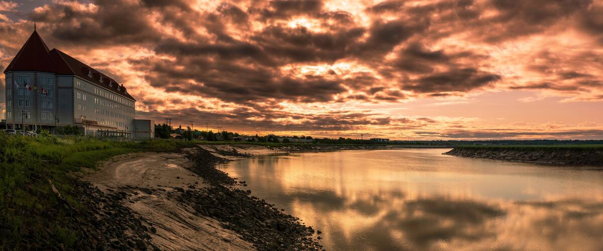 A riverside view with a large building and a dramatic sunset sky.