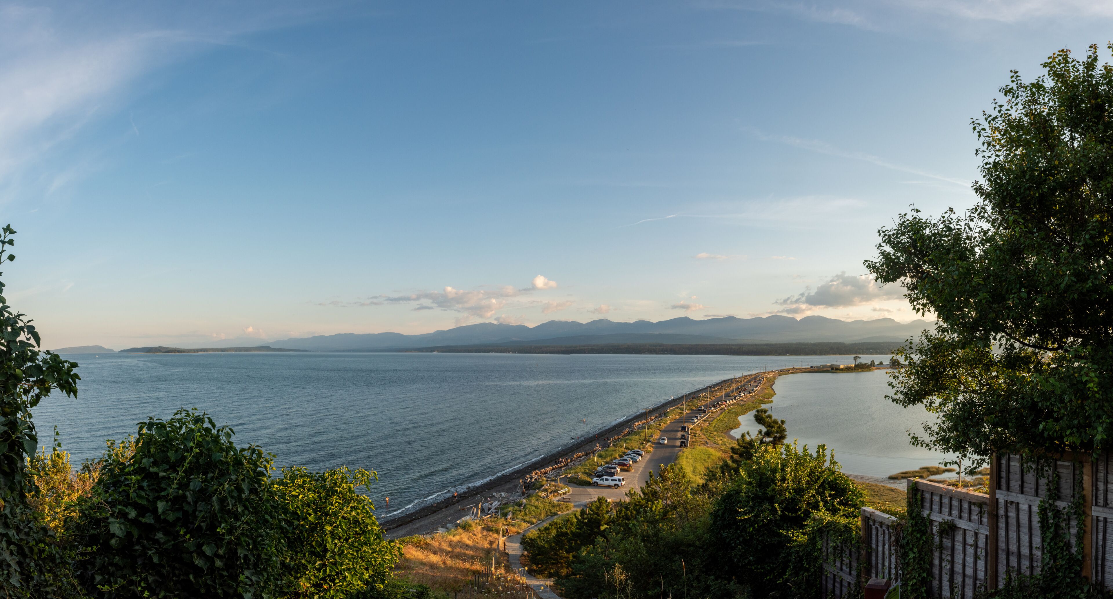 A coastal landscape with a long beach, a road parallel to the shore, and mountains in the distance.